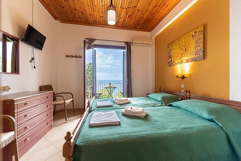 A room with twin beds and the balcony door open to the Aegean